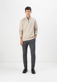 Beige zip-up sweater with long sleeves and ribbed cuffs, paired with dark gray slim-fit pants and black loafers, on a plain background.