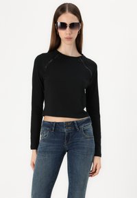 Black cropped long-sleeve top with a smooth texture, featuring zipper accents and eyelets. Paired with fitted blue denim jeans.