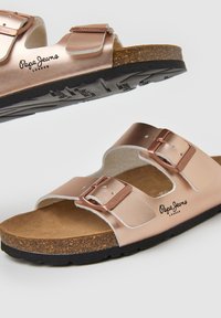 Twee metallic rosegouden sandalen met twee verstelbare banden, een kurken voetbed en een zwarte rubberen zool met een gestructureerde grip.