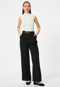 Witte mouwloze ribben top, hoge hals, gecombineerd met hoge taille zwarte wijde broek, geaccentueerd met een zwarte riem met een zilveren gesp.