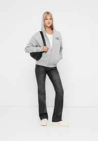 Svijetlosivi zip-up dukserica s logotipom, bijela majica, tamnosive uske traperice, i bijele tenisice. Kosa je ravna i do ramena. Crna torba.