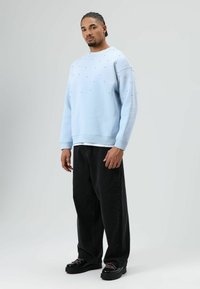 Sweat-shirt bleu clair avec petits clous, coupe décontractée. Porté avec un jean noir ample et des chaussures à plateforme noires avec des lacets colorés.