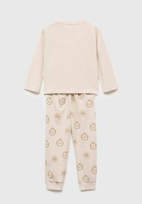 Béžové pyžamo pro batolata s dlouhým rukávem, které má jednobarevný vršek a kalhoty s opakujícím se vzorem lvích hlav v jemných hnědých a krémových odstínech.