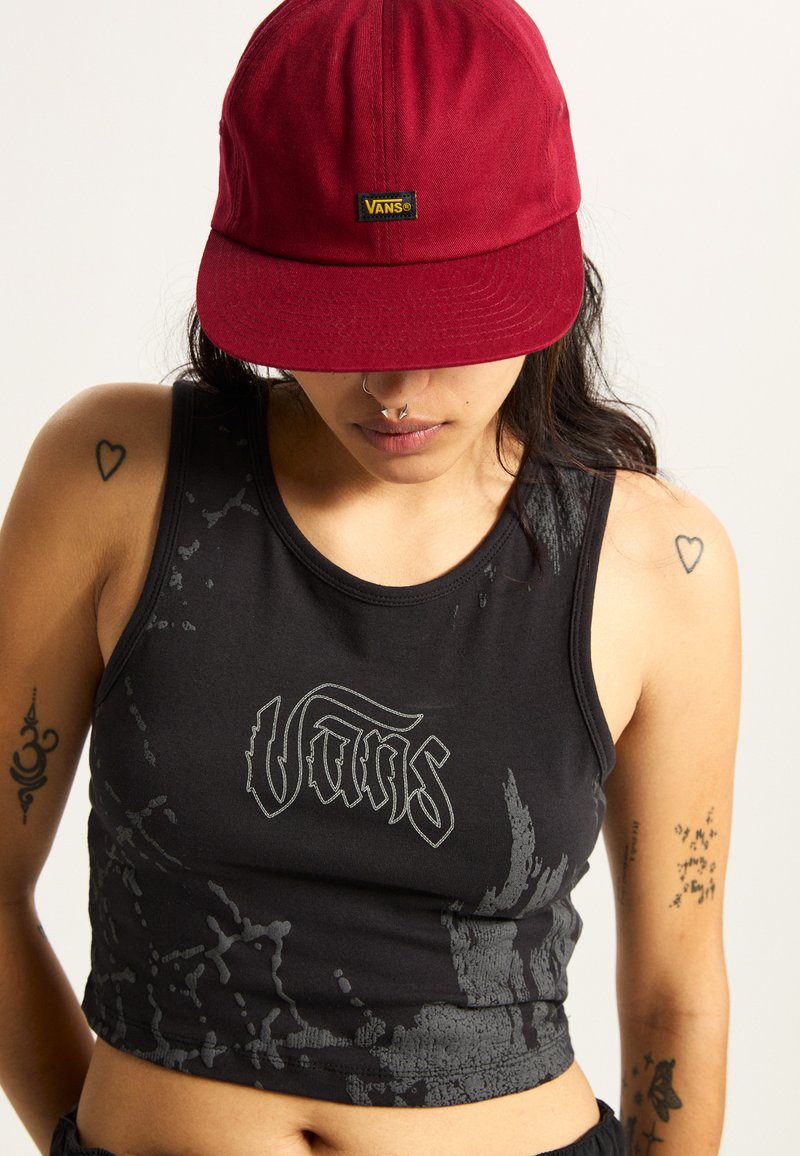 Camiseta sin mangas negra con patrón de salpicaduras grises y logo de "Vans", combinada con una gorra roja. Presenta un cuello redondo y un diseño ajustado.