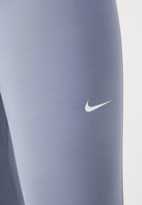 Nike tajice od mekanog mat lavande materijala, s bijelim logom na lijevoj nozi. Glatka tekstura, dizajn koji se prilagođava tijelu.