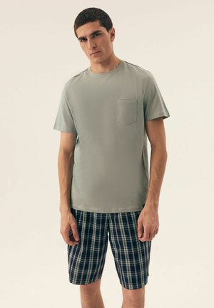 Helles grünes T-Shirt mit kurzen Ärmeln und Brusttasche, kombiniert mit karierten Shorts in Marineblau und Grün. Aus Baumwollmaterial mit entspannter Passform.