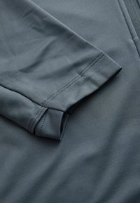 Szara część koszuli z długim rękawem wykonana z gładkiej, teksturowanej tkaniny. Zawiera starannie obszyty mankiet oraz detale szwów. Nowoczesny, dopasowany krój.