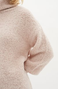 Maglione morbido e rosa chiaro con un tessuto testurizzato e peloso. Presenta un colletto alto e maniche larghe, evidenziando una vestibilità rilassata.