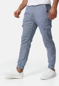 Hellblaue, strukturierte Jogginghosen mit elastischen Bündchen und Seitentaschen, kombiniert mit weißen Sneakers, die einen lässigen Schnitt und einen entspannten Stil präsentieren.