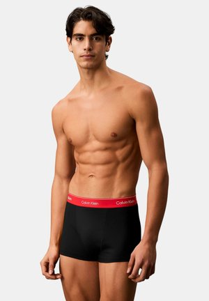 Svarta boxer briefs med en röd Calvin Klein logotyp på midjebandet. Tyget verkar slätt och passformen är åtsittande, vilket framhäver kroppens form.