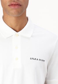 Weiße Poloshirt aus strukturiertem Baumwollstoff. Mit Kragen, drei Knöpfen und gesticktem "LYLE & SCOTT" in Schwarz auf der linken Seite.