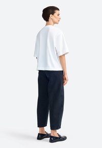 T-shirt blanc surdimensionné à manches courtes, associé à un pantalon en denim sombre et des mocassins noirs brillants. Texture en coton lisse, coupe décontractée.