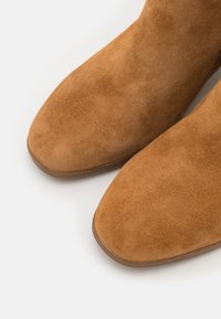 Bottines en daim couleur sable avec un bout légèrement pointu, dotées d'une texture lisse et d'un petit talon, vues de dessus.