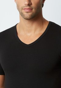 T-shirt nero a V in tessuto morbido e liscio. Presenta una forma aderente e maniche corte, con un sottile dettaglio di cucitura lungo il colletto.
