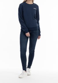 Felpa blu navy con scollo rotondo e polsini a costine; tessuto leggero; abbinata a jeans skinny scuri e sneakers bianche.