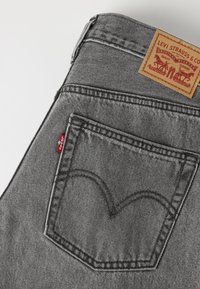 Πίσω τσέπη γκρι τζιν Levi's με κόκκινη ετικέτα Levi's και καφετί δερμάτινη επιφάνεια με το λογότυπο και κείμενο Levi Strauss.