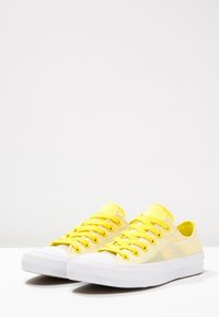 Baskets en toile jaunes avec une surface texturée, semelle en caoutchouc blanc et lacets assortis. Design classique bas.