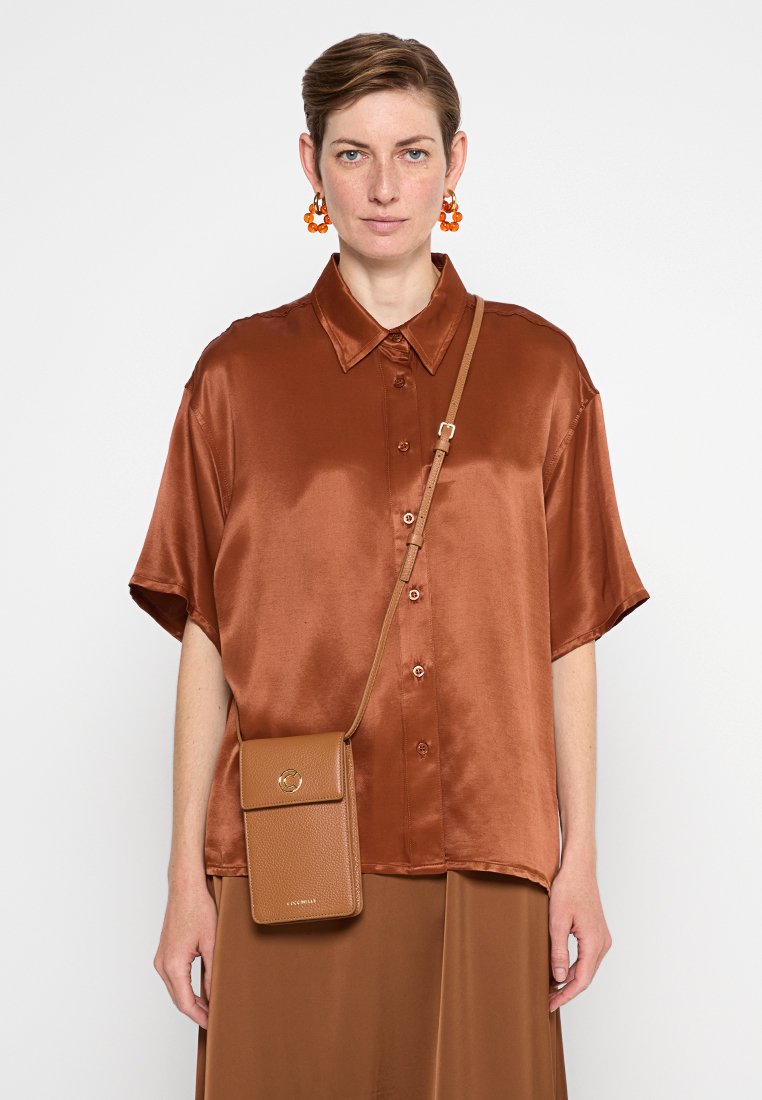 Rdzawy jedwabny krótki rękaw koszula z guzikami, w połączeniu z beżową torbą crossbody, wyróżniającą się teksturowanym materiałem i okrąłym akcentem z metalowego zamiast.