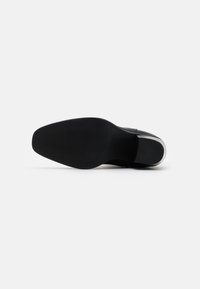 Suela de zapato negra con una superficie estriada para agarre, con un talón liso y borde de suela blanca. Diseño minimalista sin patrones visibles.
