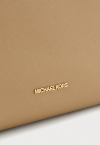 Portofel texturat în nuanță de tan, cu o suprafață netedă, având un logo auriu "Michael Kors" pe față pentru a evidenția marca.