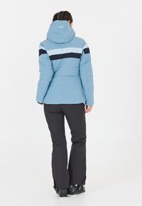 Lyseblå dunjakke med navy vandrette striber, aftagelig hætte og lynlåslommer, sammen med sorte snebukser og støvler.