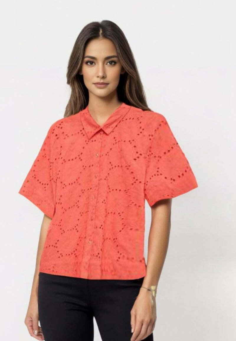 Korallfarget kortermet skjorte med øyeletdesign, knappestolpe og krage. Brukt med svarte bukser, noe som skaper en fargekontrast.
