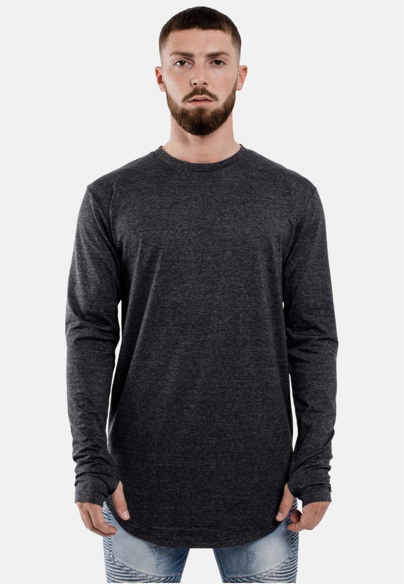 Langsleeve, donkergrijze t-shirt met een ronde hals, zachte textuur en verlengde zoom. Gepaard met versleten lichtblauwe jeans.
