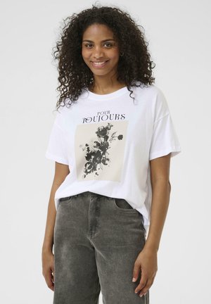 White cotton t-shirt featuring a black floral print on a beige background. Simple crew neck and relaxed fit, paired with gray jeans.