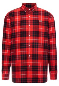 Camisa de manga larga a cuadros rojos y negros hecha de algodón. Cuenta con un collar de botones, botones frontales y un pequeño logotipo bordado en el pecho.