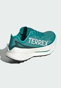 Zielone buty sportowe z siateczkową cholewką, białym logo "TERREX", amortyzowaną podeszwą i czarną gumową podeszwą; zaprojektowane dla wydajności i stabilności.