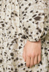 Robe à imprimé léopard dans des teintes beige clair et marron, dotée de manches bouffantes et d'une taille froncée, fabriquée en tissu doux et texturé.