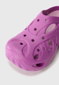 Sabots légers de couleur violette en matériau synthétique texturé, dotés de trous de ventilation et d'une semelle crantée épaisse pour une meilleure adhérence.
