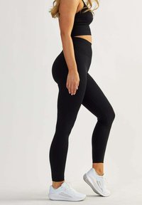 Black ribbed leggings with a high waistband, paired with white athletic shoes. The fabric appears soft, with a smooth texture and fitted design.