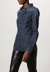 Denimskjorta med knappar, mörkblå med ljusare prickar, med spetsig krage och långärmar. Skuren passform och mjuk textur.