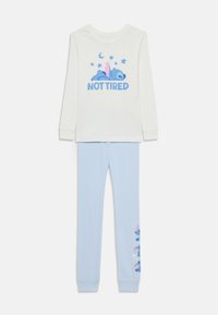 Haut à manches longues blanc avec le texte bleu "NOT TIRED" et un graphique. Pantalon de pyjama bleu clair avec une finition texturée et un motif de personnage de dessin animé.
