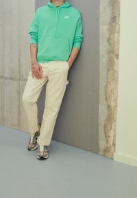 Turkos Nike hoodie, vita cargobyxor och grå sneakers med gröna detaljer. Släta texturer med kontrasterande färger och avslappnad passform.