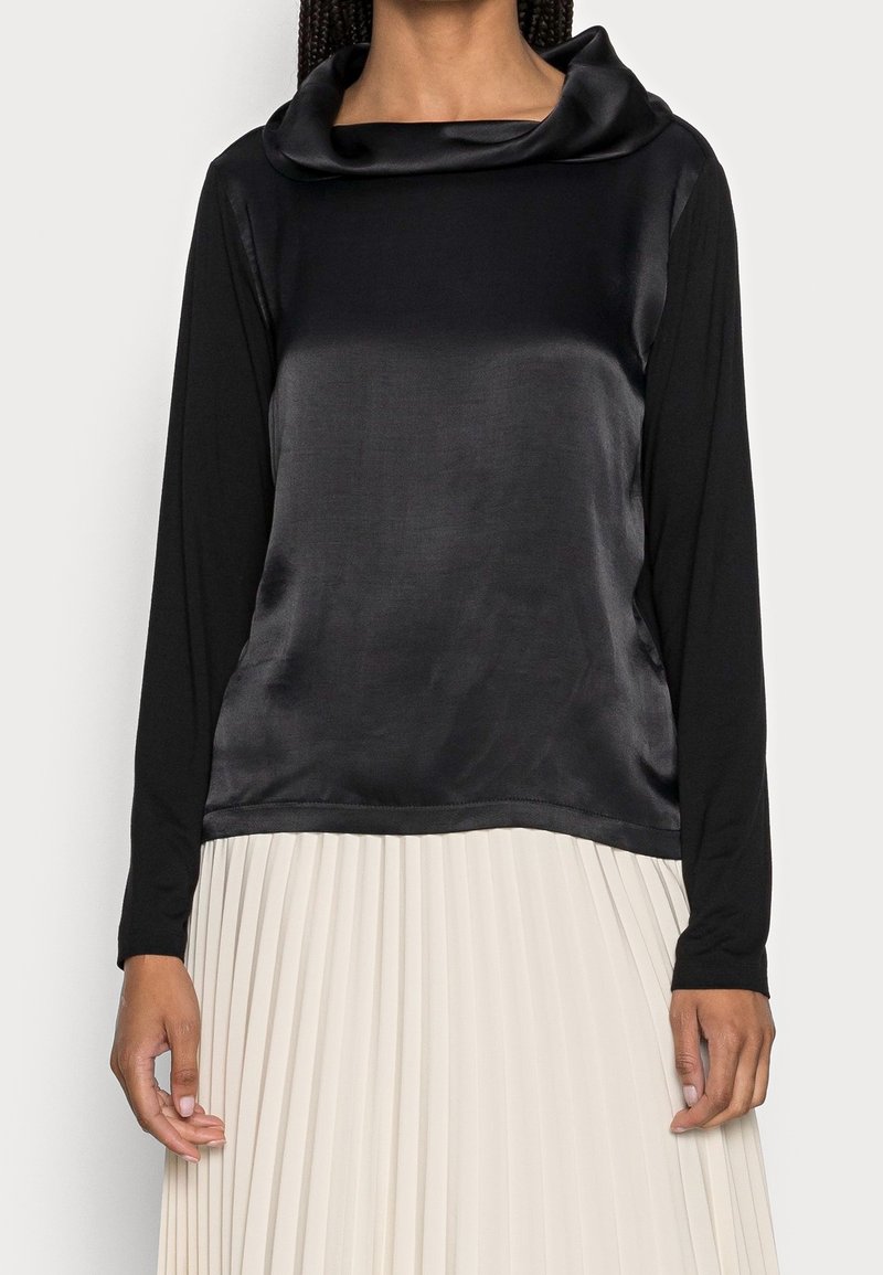 Mustapaita, jossa on pitkät hihat ja satiininen kauluspanta. Materiaali kontrastoi laskostetun, vaalean alaosan kanssa. Suojaava rakenne.