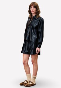 Zwart faux leren shirt en rok set, met een kraagontwerp en knoopaccenten, gecombineerd met schoenen met luipaardprint en beige sokken.