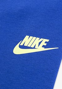 Mėlyna tekstilė su tekstūruotu paviršiumi, centre akcentuota geltona Nike logo ir šūvis.