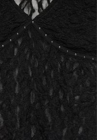 Tissu en dentelle noire avec motifs floraux, avec une couture décorée de petits clous argentés le long du bord.