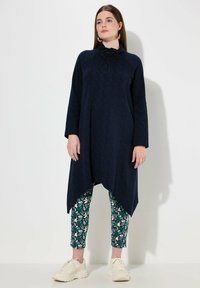 Tunic navy con collo alto e cordoncino, caratterizzata da un motivo sottile. Abbinata a leggings cropped con stampa floreale e sneaker bianche.