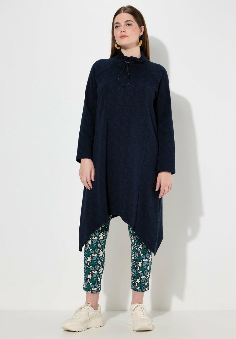 Tunic navy con collo alto e cordoncino, caratterizzata da un motivo sottile. Abbinata a leggings cropped con stampa floreale e sneaker bianche.