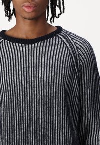 Navy- und weiß gestreifter Strickpullover mit geripptem Textur und Rundhalsausschnitt. Das Design umfasst Raglanärmel in kontrastierenden Farben.