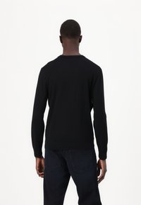 Maglione nero a maniche lunghe realizzato in un tessuto a maglia morbida, con scollatura a girocollo e polsini aderenti, abbinato a jeans in denim scuro.