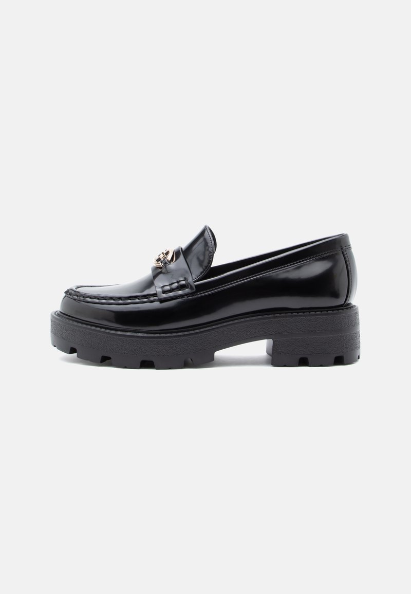 Mocassino in pelle patent nera con suola spessa e testurizzata nera, dotato di un accento decorativo sulla tomaia e un design della punta arrotondata.
