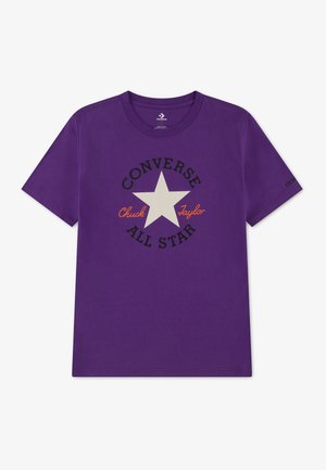 T-shirt violet à manches courtes avec une étoile blanche et le texte "Converse All Star Chuck Taylor" sur la poitrine, et un petit logo sur la manche droite.