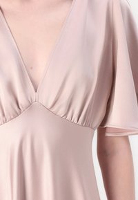 Abito rosa pallido con scollatura a V profonda, maniche a sbuffo corte e dettagli gathered sul busto, realizzato in un tessuto leggero e morbido.