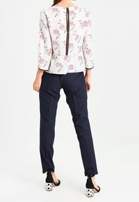 Blusa floreale con zip sul retro, maniche a tre quarti, abbinata a pantaloni blu navy e tacchi neri con pois bianchi.