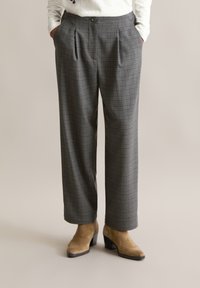 Grijze geruite broeken met een hoge taille, voorplooien en een loose fit. De stof heeft een gladde textuur en is gecombineerd met lichtbruine haklaarzen.