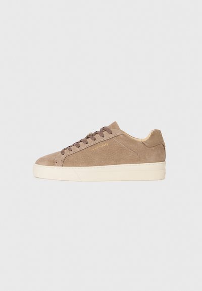 Beige suède sneaker met een ronde neus, crèmekleurige rubberen zool en bruine veters. Beschikt over een reliëf merklogo aan de zijkant en textielmateriaal.
